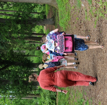 Leerkracht wendelt met een groep leerlingen op wandelpad tussen het groen